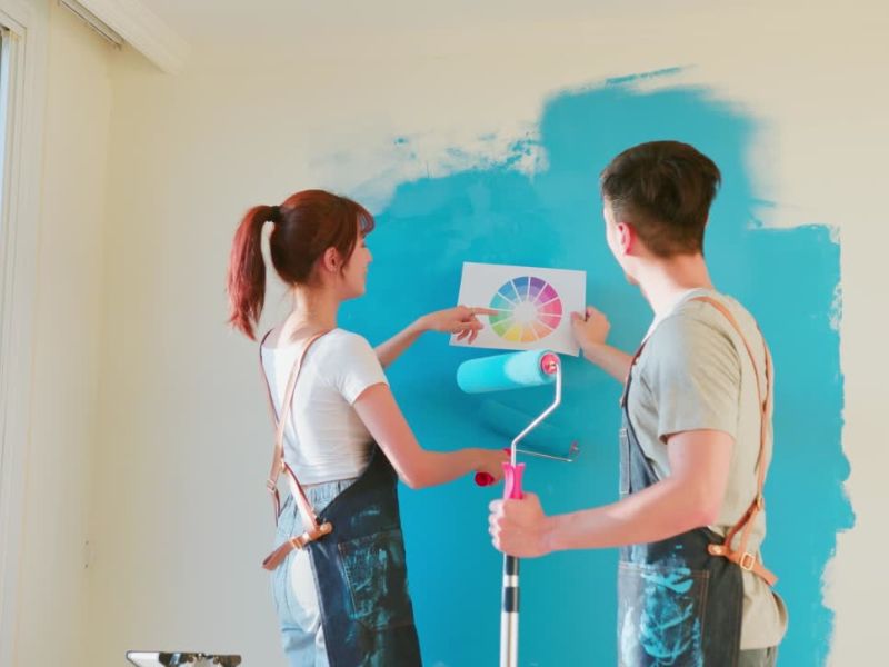 momak i devojka drže papir sa različitim nijansama boja i kreče svoj zid u plavu boju